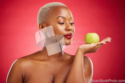 Image of Black woman, apple and thinking for natural nutrition or healthy diet against a red studio background. African female person palm with natural organic green fruit for food snack, health and wellness