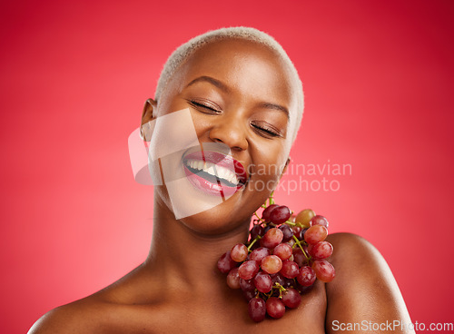 Image of Beauty, smile and grapes with a model black woman in studio on a red background for health or nutrition. Skincare, happy and fruit with a young female person posing for wellness, diet or detox