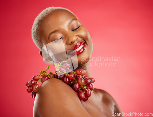 Image of Skincare, smile and grapes with a model black woman in studio on a red background for health or nutrition. Beauty, happy and fruit with a young female person posing for wellness, diet or detox