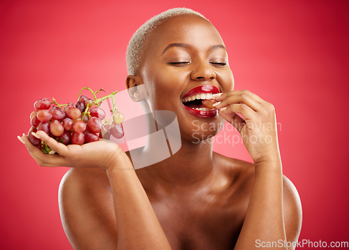 Image of Health, eating and a black woman with grapes on a red background for nutrition or diet. Smile, beauty and an African model or girl with fruit, hungry and food for a detox isolated on a backdrop