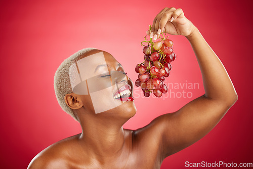 Image of Happy, eating and black woman with grapes on a red background for nutrition, diet or health. Smile, beauty and an African model or girl with fruit, hungry and food for a detox isolated on a backdrop