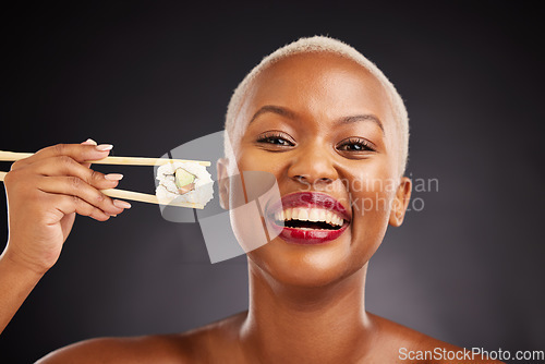 Image of Face, woman and sushi with chopsticks in studio for healthy eating, beauty and food. Portrait of a happy black female model with makeup on a dark background for healthy eating, diet or seafood