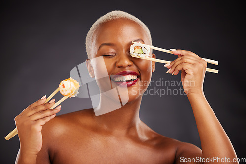 Image of Sushi, face and woman with chopsticks in studio for healthy eating, beauty glow and food. Black female aesthetic model with makeup on a dark background for wellness, funny diet or seafood advertising