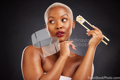 Image of Face, thinking and woman with sushi and chopsticks in studio for healthy eating, beauty or food. Black female model with makeup idea on dark background for wellness glow, diet or seafood advertising