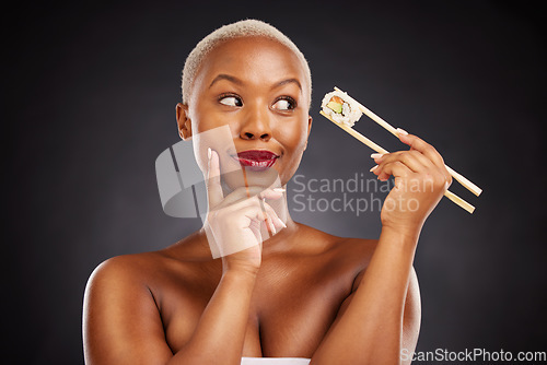 Image of Sushi, thinking and face of a woman with chopsticks in studio for healthy eating, beauty or food. Black female model with makeup on dark background for wellness glow, diet or seafood advertising idea