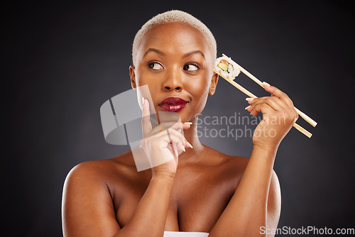 Image of Thinking, idea and woman with sushi and chopsticks in studio for healthy eating, beauty or food. Black female model with makeup on dark background for wellness glow, diet or seafood advertising