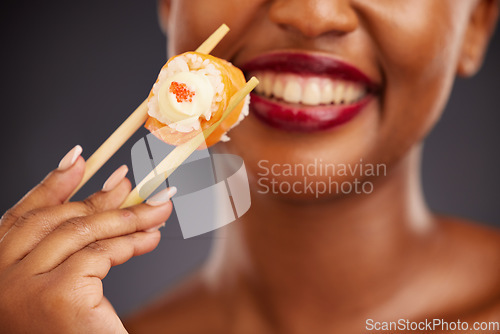 Image of Sushi, chopsticks and mouth of a woman in studio for healthy eating, salmon or food. Black female model with makeup and smile on a dark background for wellness, diet or seafood advertising in hand