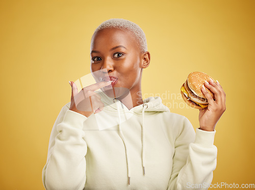 Image of Burger, eating and portrait of woman or student on studio yellow background for restaurant promotion or deal. Hungry and happy, african person or customer experience with fast food or hamburger taste