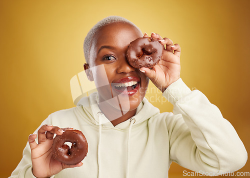 Image of Portrait, chocolate and donut with a black woman in studio on a gold background for candy or unhealthy eating. Smile, food and baking with a happy young female person holding sweet pastry for dessert