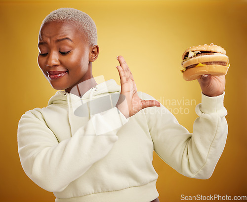 Image of Diet, reject and fast food with woman or nutrition in yellow background is unhappy. Burger, no and girl is frustrated with choice in studio with mistake or refuse with meal for weight or health.