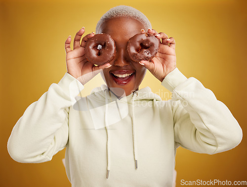 Image of Face, chocolate and donut with a black woman in studio on a gold background for candy or unhealthy eating. Smile, food and baking with an excited young female person holding sweet pastry for dessert