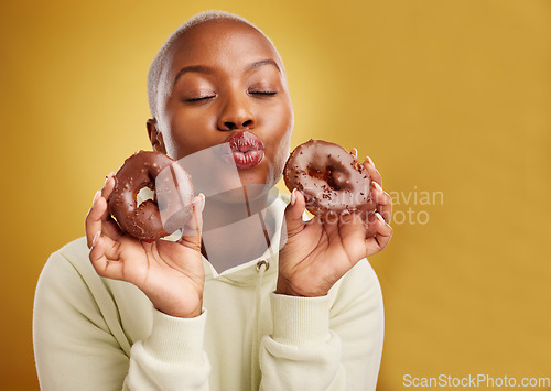 Image of Face, kiss and donut with a black woman in studio on a golden background for candy or unhealthy eating. Pout, food and baking with a cute young female person holding sweet pastry for dessert