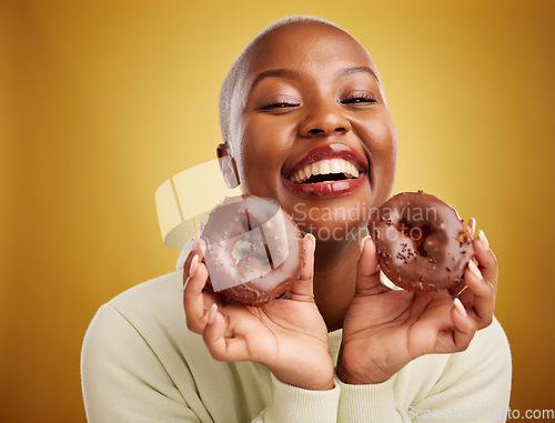 Image of Portrait, food and donut with a black woman in studio on a gold background for candy or unhealthy eating. Smile, chocolate and baking with a happy young female person holding sweet pastry for dessert