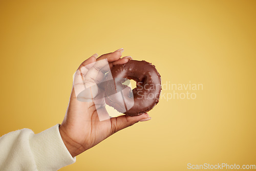 Image of Hand, donut and chocolate dessert in studio for unhealthy eating, sugar or cake advertising. Closeup of a person with a doughnut on a yellow background for junk food, diet calories or fun emoji