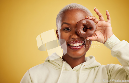 Image of Portrait, chocolate and donut with a black woman in studio on a gold background for candy or unhealthy eating. Eye, food or baking with an excited young female person holding sweet pastry for dessert