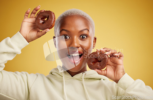 Image of Portrait, chocolate and donut with a black woman in studio on a gold background for candy or unhealthy eating. Smile, food and baking with a happy young female person holding sweet pastry for dessert