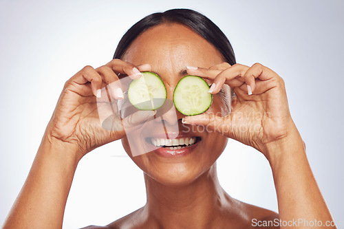 Image of Cucumber, face and beauty of woman in studio, white background and aesthetic glow. Happy female model, natural skincare and fruits on eyes for sustainable cosmetics, vegan dermatology and nutrition