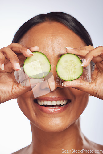 Image of Cucumber, face and skincare of happy woman in studio, white background and aesthetic shine. Female model, natural beauty and fruits on eyes for sustainable cosmetics, vegan dermatology and nutrition