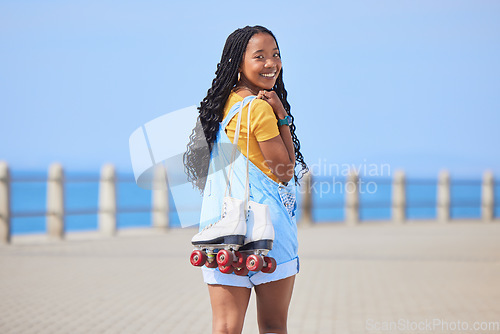 Image of Portrait, back and roller skating with a black woman by the sea, on the promenade for training or recreation. Beach, sports or fun with a happy young teenager holding skates on the coast by the ocean