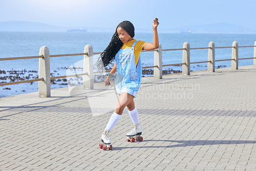 Image of Roller skating, fun or freedom with a black woman by the sea, on the promenade for training or recreation. Beach, sports and a young female teenager in skates on the coast by the ocean or water