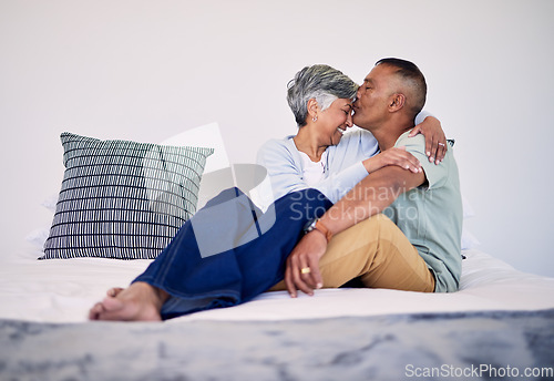 Image of Love, kiss and senior couple on their bed in their home while relaxing, bonding and spending time together. Happy, affection and elderly man and woman in retirement resting in bedroom in their house.