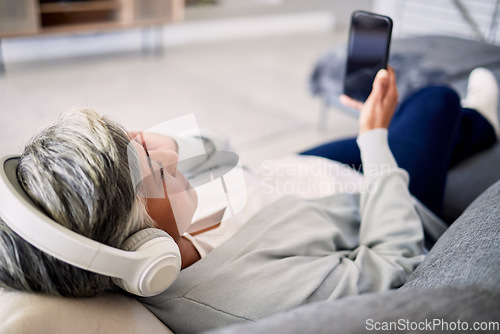 Image of Senior woman, headphones and phone on sofa, relax and music in home living room with search, choice and listening. Elderly lady, smartphone and audio streaming app for radio, podcast and lounge couch