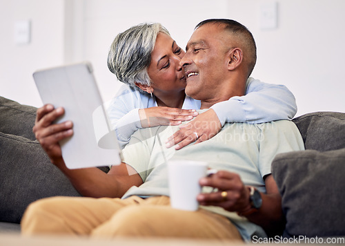 Image of Senior couple, hug and tablet on sofa to relax with quality time in home with kiss during retirement. Couple, technology and embrace with elderly man or woman in living room together on couch.