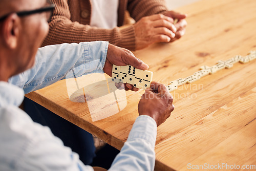 Image of Hands, dominoes and a senior man playing a game at a table in the living room of a retirement home. Thinking, strategy and fun with an elderly male pensioner in a house closeup for entertainment