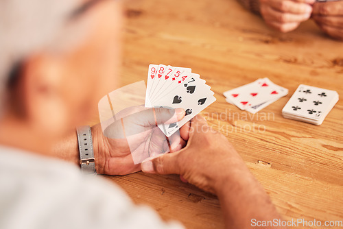 Image of Hands, cards and a senior man playing poker at a table in the living room of a retirement home. Gambling, planning and fun with an elderly male pensioner in a house closeup for entertainment games