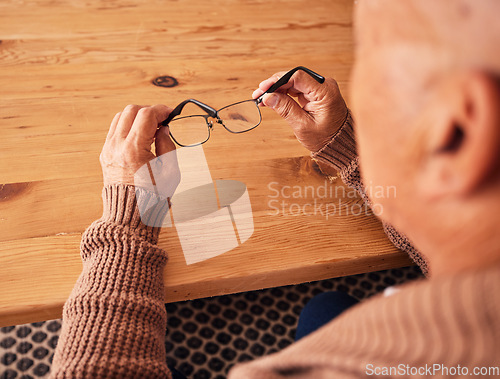 Image of Senior man, hand holding glasses and eye care with vision, prescription lens and designer frame at table. Elderly guy, hands and spectacles for vision, eyesight and health at desk in retirement home