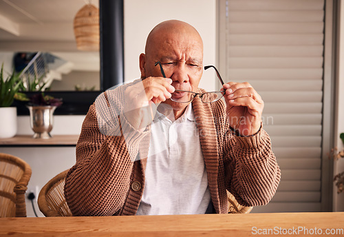 Image of Glasses, vision and a senior man at a table in the living room of his home during retirement. Thinking, relax and eyesight with an elderly male person holding prescription frame lenses in his house