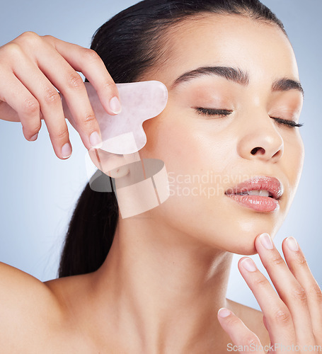 Image of Gua sha, massage and asian woman with skincare tool in studio for anti aging, circulation or fine lines on grey background. Rose quartz, beauty and lady model with face crystal or lymphatic drainage