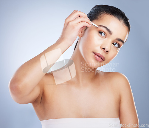 Image of Young woman tweezing her eyebrows in a studio for grooming or hair removal face routine. Skincare, beauty and female model doing a facial epilation treatment with tweezers isolated by gray background