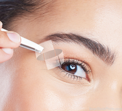 Image of Closeup of a young woman tweezing her eyebrows in a studio for grooming or hair removal face routine. Skincare, beauty and zoom of female model doing a facial epilation treatment with metal tweezers.