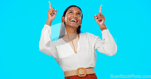 Image of Excited, happy and woman pointing up at mockup showing deal, sale and branding isolated in a studio blue background. Smile, fashion and portrait of Indian female show product placement or logo