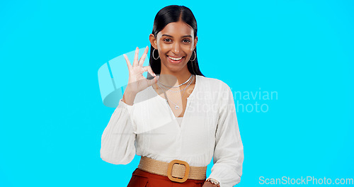 Image of Ok, perfect and happy woman with hand gesture for success, approval and isolated in studio blue background. Emoji, face and portrait of Indian female with fashion, perfection and support review