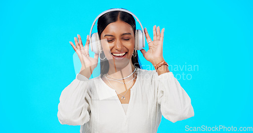 Image of Face, music and Indian woman with headphones, streaming and happiness against blue studio background. Portrait, female and lady with headset, listening to song and dancing with success and celebrate