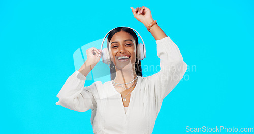 Image of Face, music and Indian woman with headphones, streaming and happiness against blue studio background. Portrait, female and lady with headset, listening to song and dancing with success and celebrate