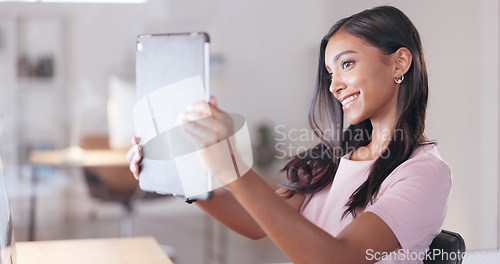 Image of Young happy woman taking a selfie with a digital tablet while relaxing in an office at work. One smiling female student taking pictures to post on social media while sitting alone in a library