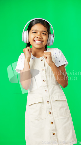 Image of Children, music and dance with a girl on a green screen background in studio streaming audio. Portrait, smile and fun with an adorable little girl dancing while listening to the radio on headphones