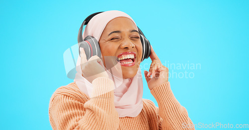 Image of Happy woman, headphones and dancing isolated on blue background listening to music for celebration and singing . Funny, dance and muslim, gen z or hijab person with streaming technology in studio