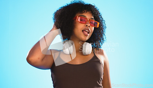 Image of Face wink, sunglasses and hair care of woman in studio isolated on a blue background. Gen z portrait, retro shades and happy mixed race female model with salon treatment for beauty and headphones.