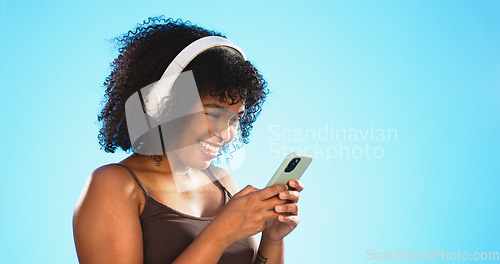 Image of Black woman, phone and headphones isolated on blue background listening to music, social media video or funny meme. Happy gen z person laughing for audio tech, internet post and cellphone in studio