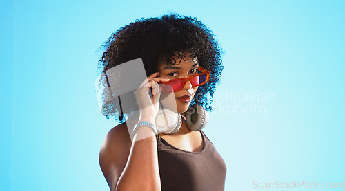 Image of Face, sunglasses and beauty of woman in studio isolated on a blue background. Fashion portrait, smile shades and happy mixed race female model with trendy, stylish or retro, cool or gen z headphones.