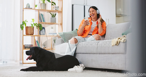 Image of Phone, headphones and laughing woman with dog on sofa in home living room. Comic, relax and happy female streaming music, radio or podcast with smartphone while playing with animal, pet or bonding.