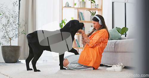 Image of Headphones, dog licking and woman in a living room feeling puppy love from pet care in a home. House, animal and young female listening to music with happiness and bonding from labrador attention