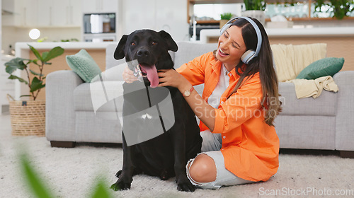 Image of Headphones, dog petting and woman in a living room feeling puppy love from pet care in a home. House, animal and young female listening to music with happiness and bonding from labrador attention