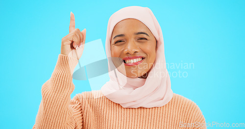 Image of Happy muslim, woman and pointing finger portrait with space for mockup, advertising or promotion. Islamic female with hand, smile and hijab for announcement, Allah or God and sale on blue background