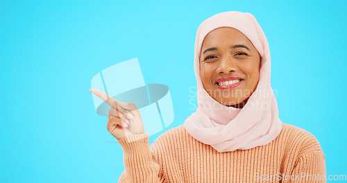 Image of Woman, pointing finger and space for happy muslim announcement with hand for mockup. Islamic female with hijab and face with smile for sale, promotion or product placement on studio blue background