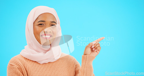 Image of Muslim woman, happy and portrait pointing finger at space for mockup, advertising or promotion. Islam female with hand, smile and hijab for product placement announcement or sale on blue background